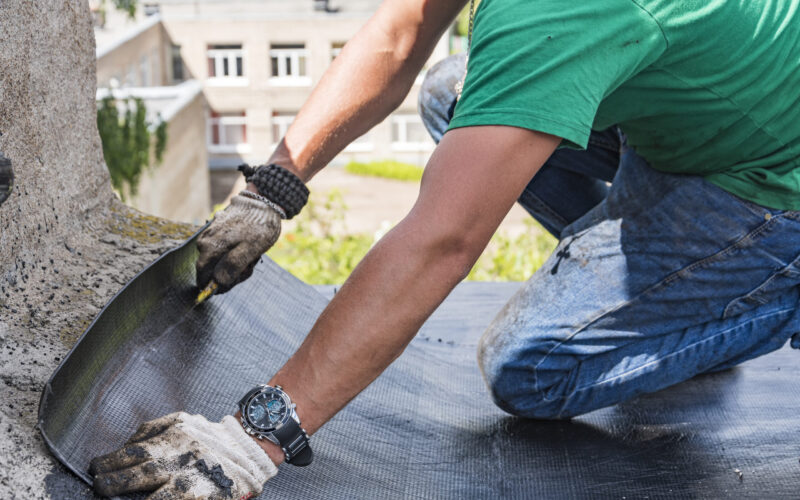 A construction worker cuts waterproofing material and prepares it for installation. Overhaul of the roof of the house.